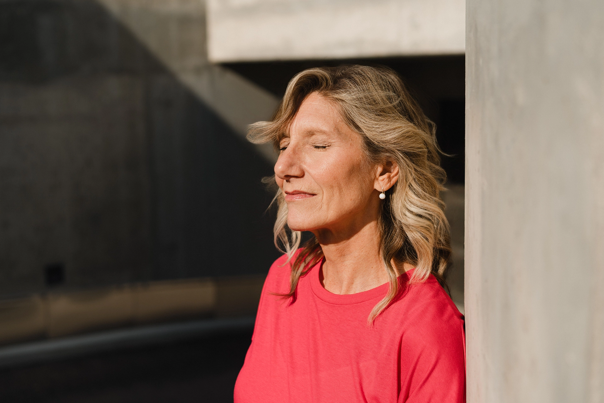 Portrait von Katja Hartmann. Sie hat die Augen in der Sonne geschlossen und lehnt an einer Wand